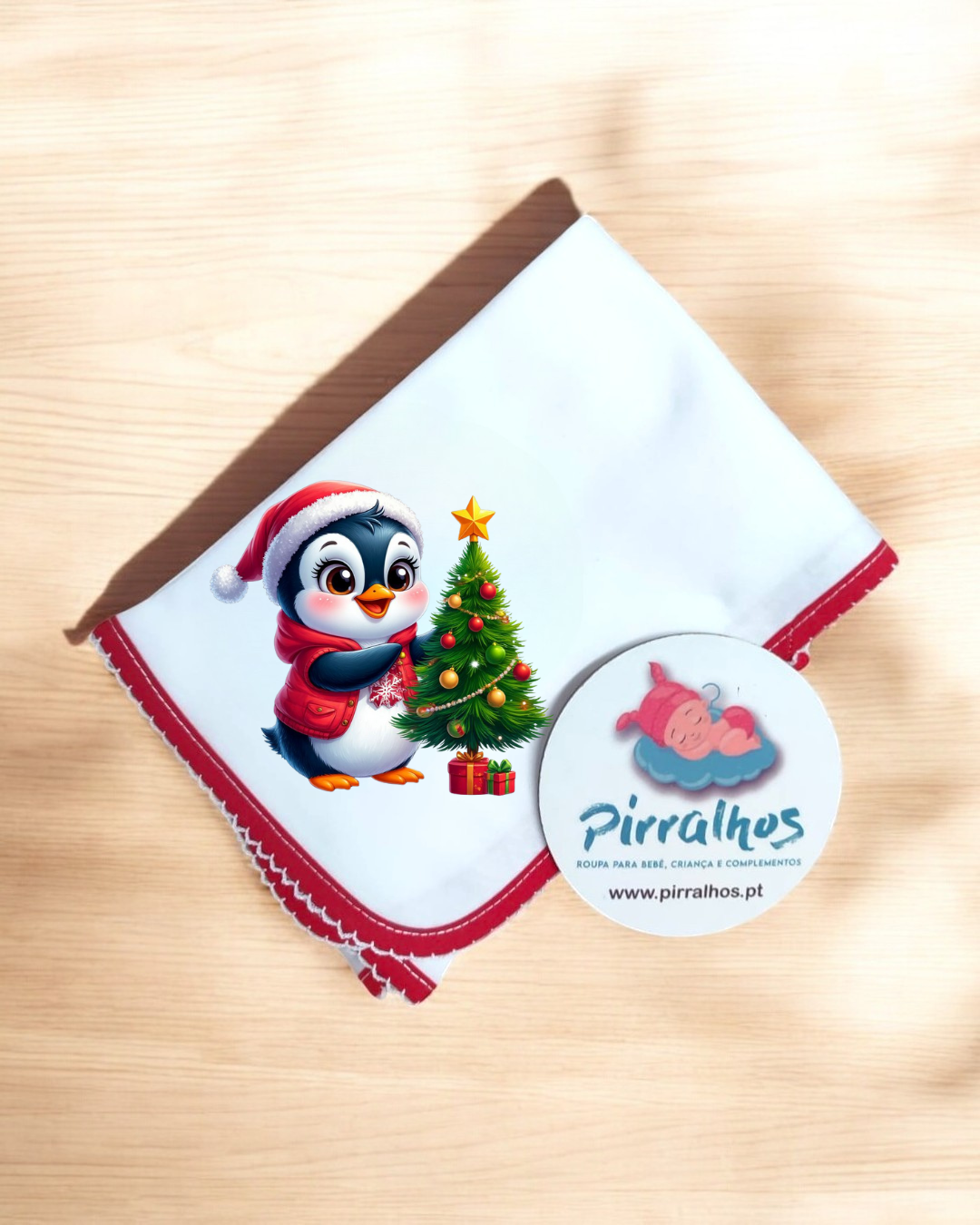Toalha branca com borda vermelha e desenho de pinguim natalício com árvore de Natal, etiqueta da marca Pirralhos
