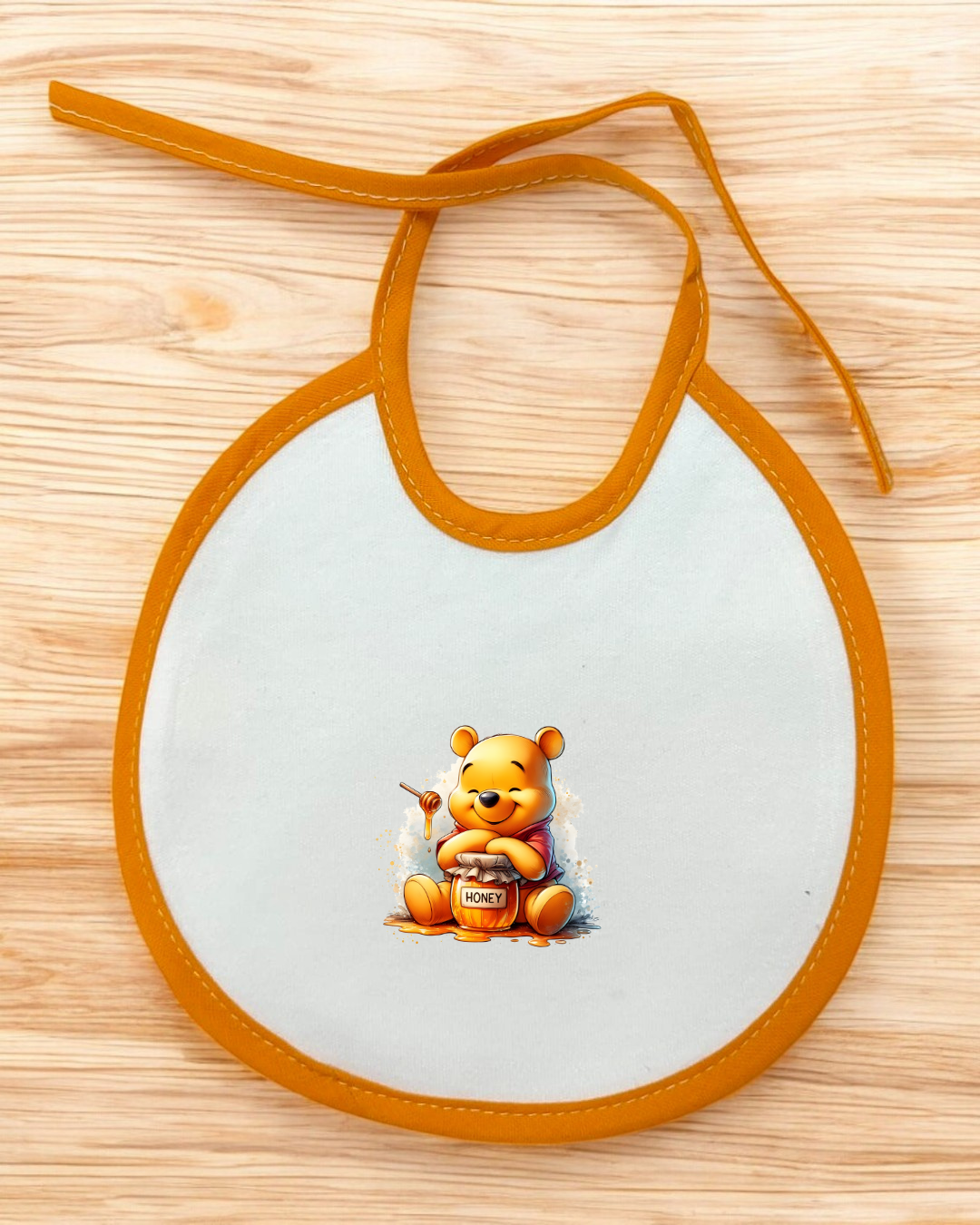 Babete branco com borda laranja e imagem do ursinho Pooh sentado com pote de mel.