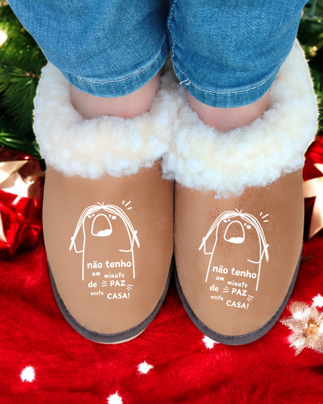 Chinelos castanhos com interior felpudo branco e texto humorístico, calças de ganga, fundo natalício