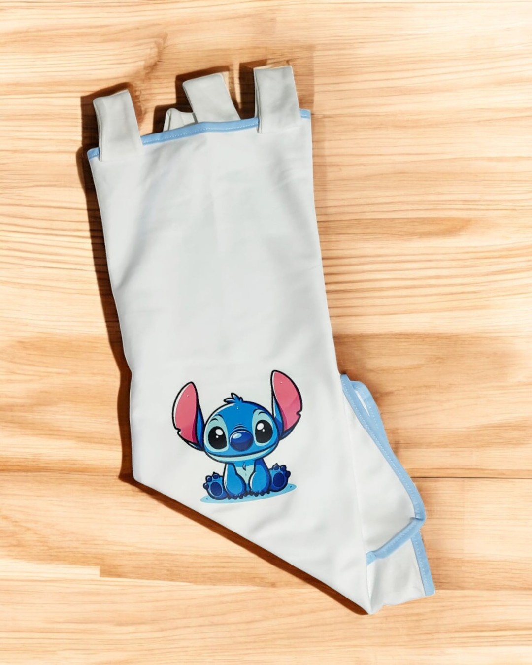Mangueira de banho infantil branca com bordas azuis e estampa do Stitch sobre madeira clara