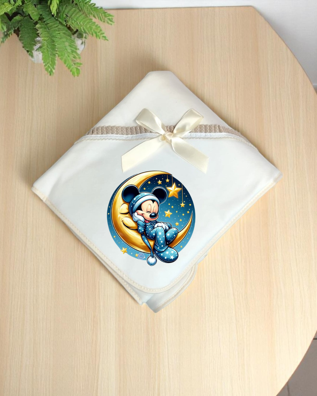 Manta branca com laço creme e estampa de personagem animado sentado numa lua amarela