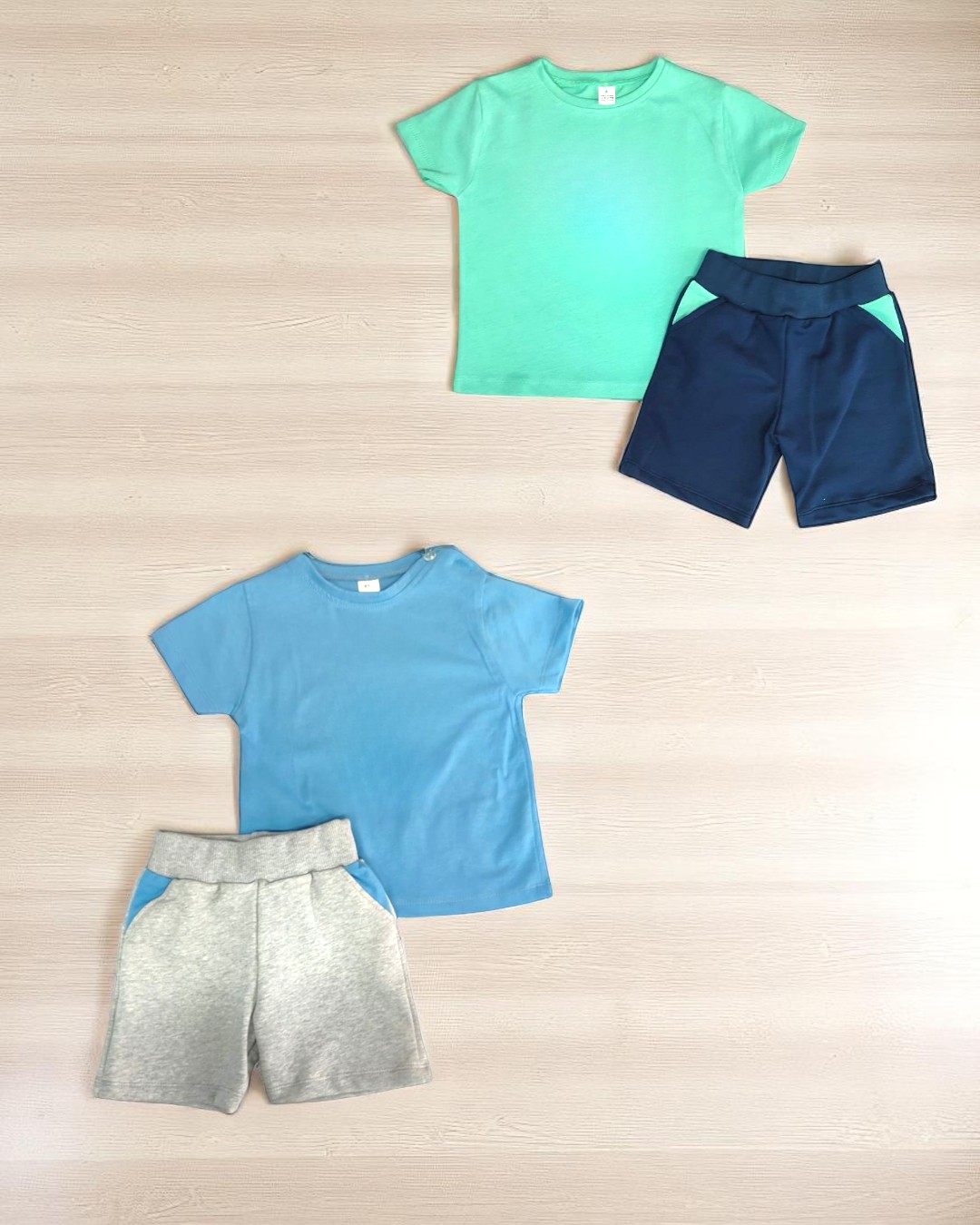 Dois conjuntos de roupa infantil com t-shirts e calções em várias cores sobre madeira clara