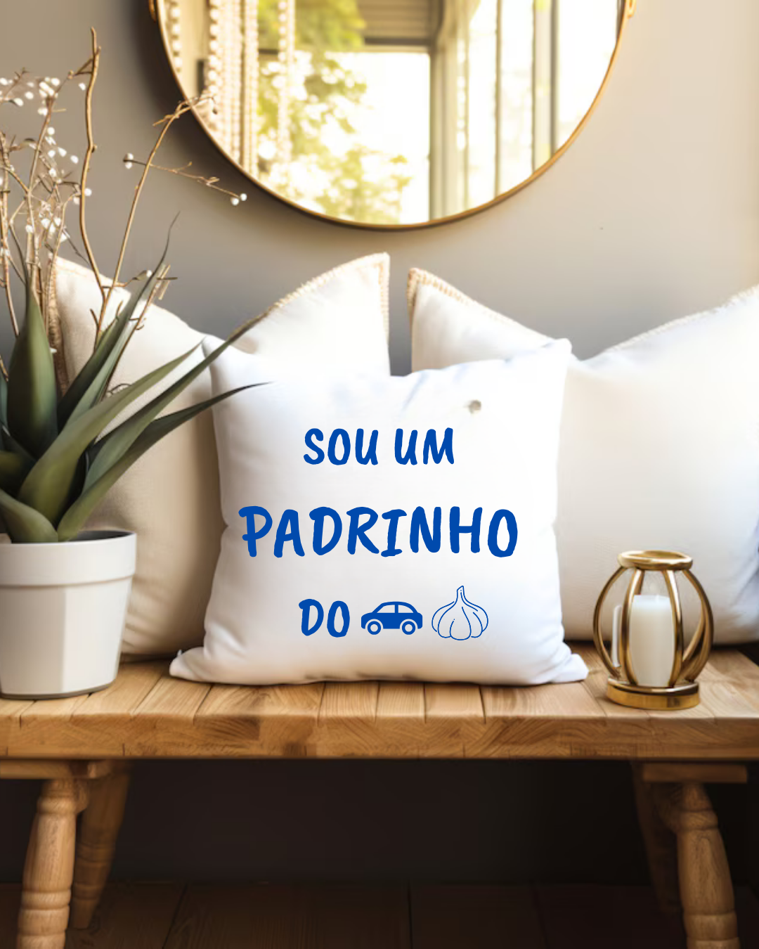 Almofada branca com texto azul 'SOU UM PADRINHO DO' e ícones de carro e alho num ambiente com planta e castiçal