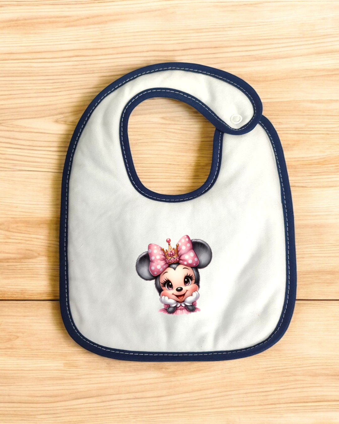 Babete branco com bordadura azul e personagem ilustrada com laço cor-de-rosa.