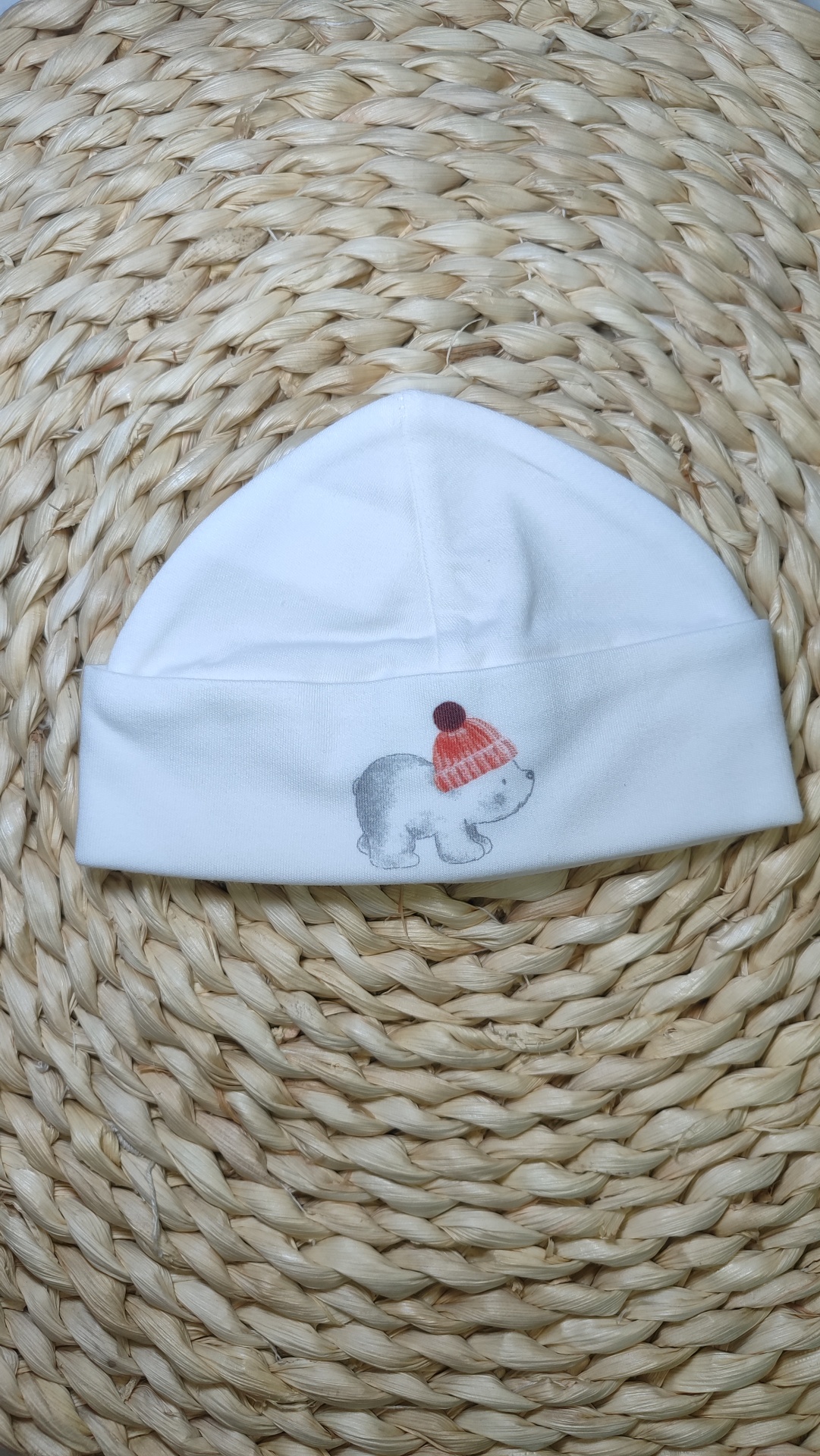 Gorro branco para bebé com desenho de urso e gorro vermelho sobre superfície trançada