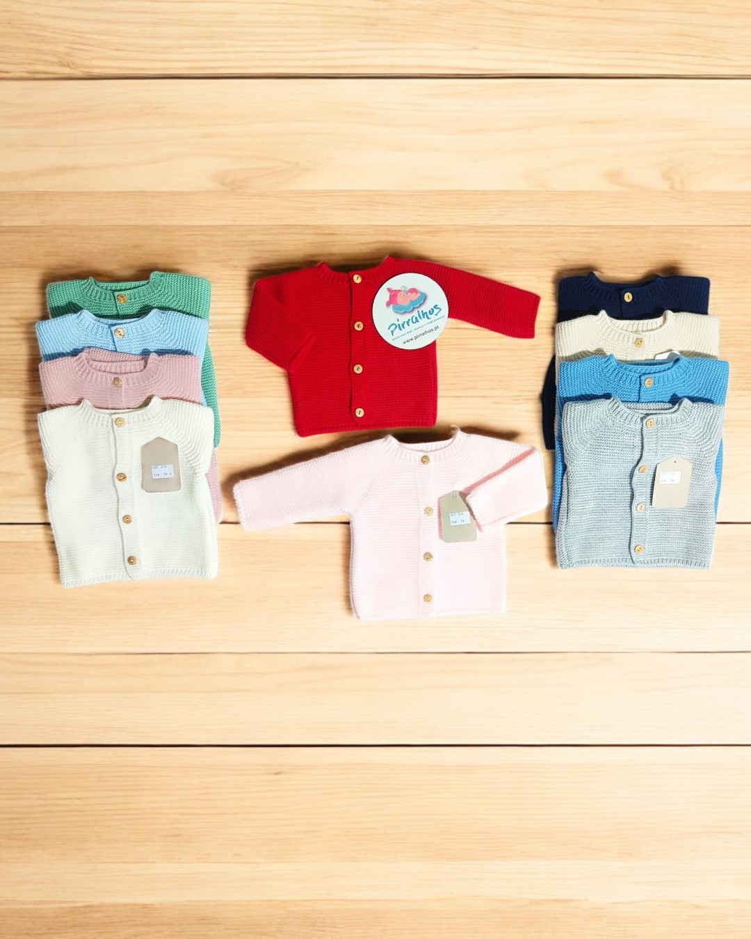 Camisolas de malha para bebé em várias cores com botões e etiquetas sobre madeira clara