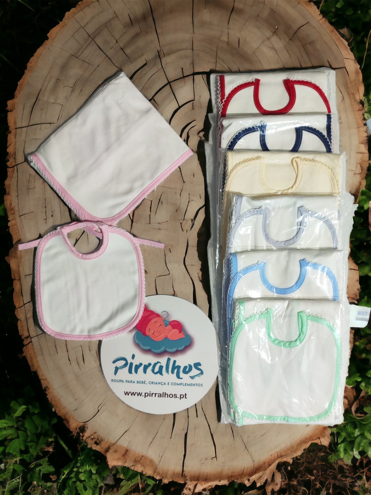 Conjunto de babetes e fralda brancos com bordas coloridas sobre tronco de árvore