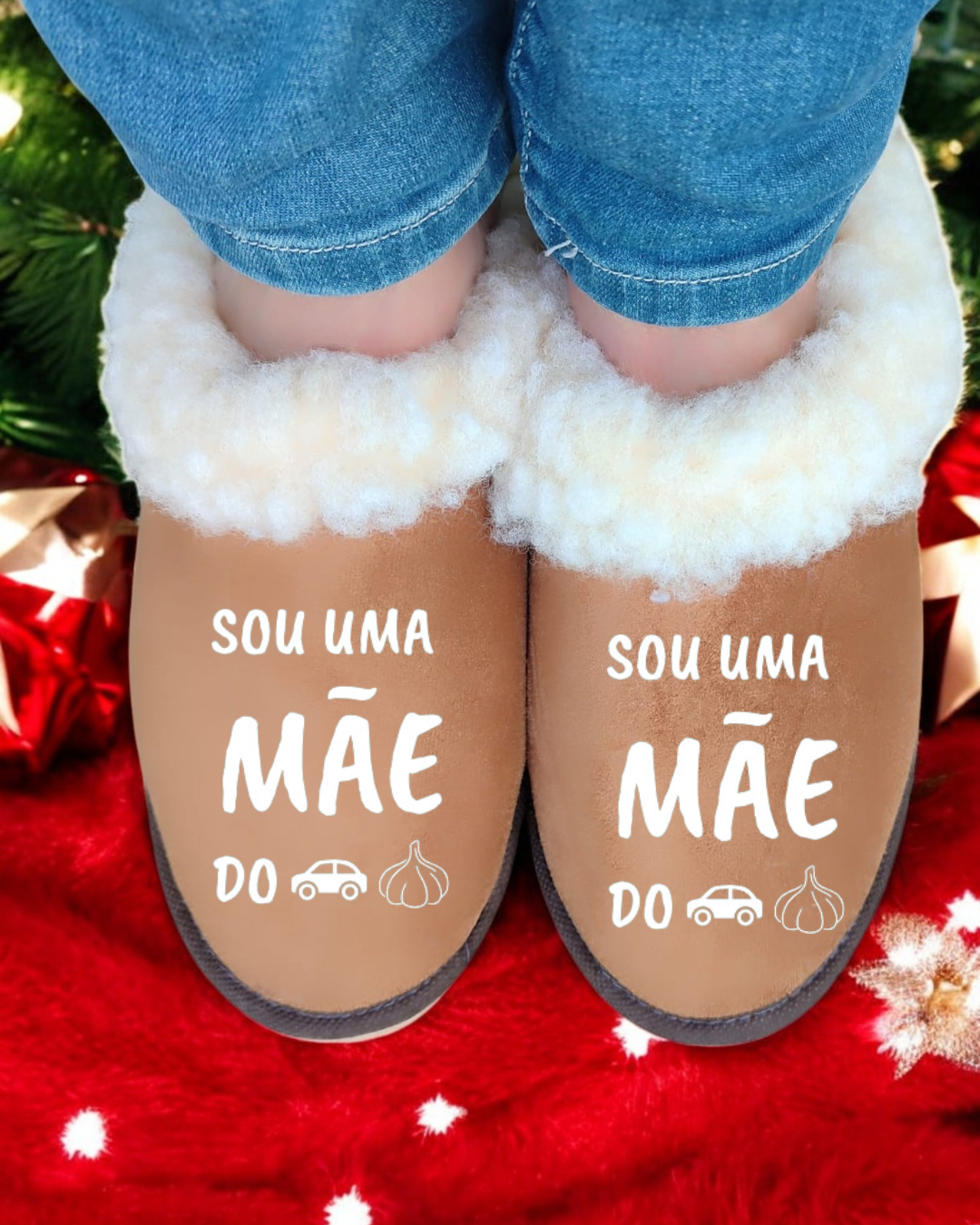 Chinelos marrons com forro branco felpudo e texto branco, usados com calças de ganga, sobre tapete vermelho festivo