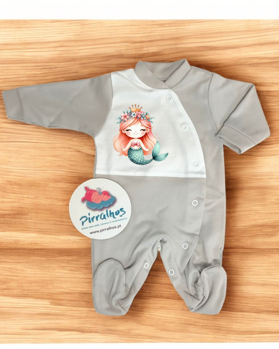 Macacão de bebé cinzento e branco com estampa de sereia e botões de pressão, sobre madeira clara