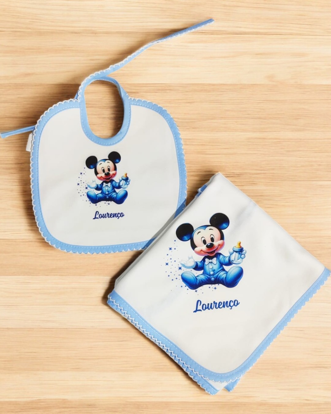 Babete e fralda com bordas azuis e estampa do Mickey Mouse bebé com o nome Lourenço