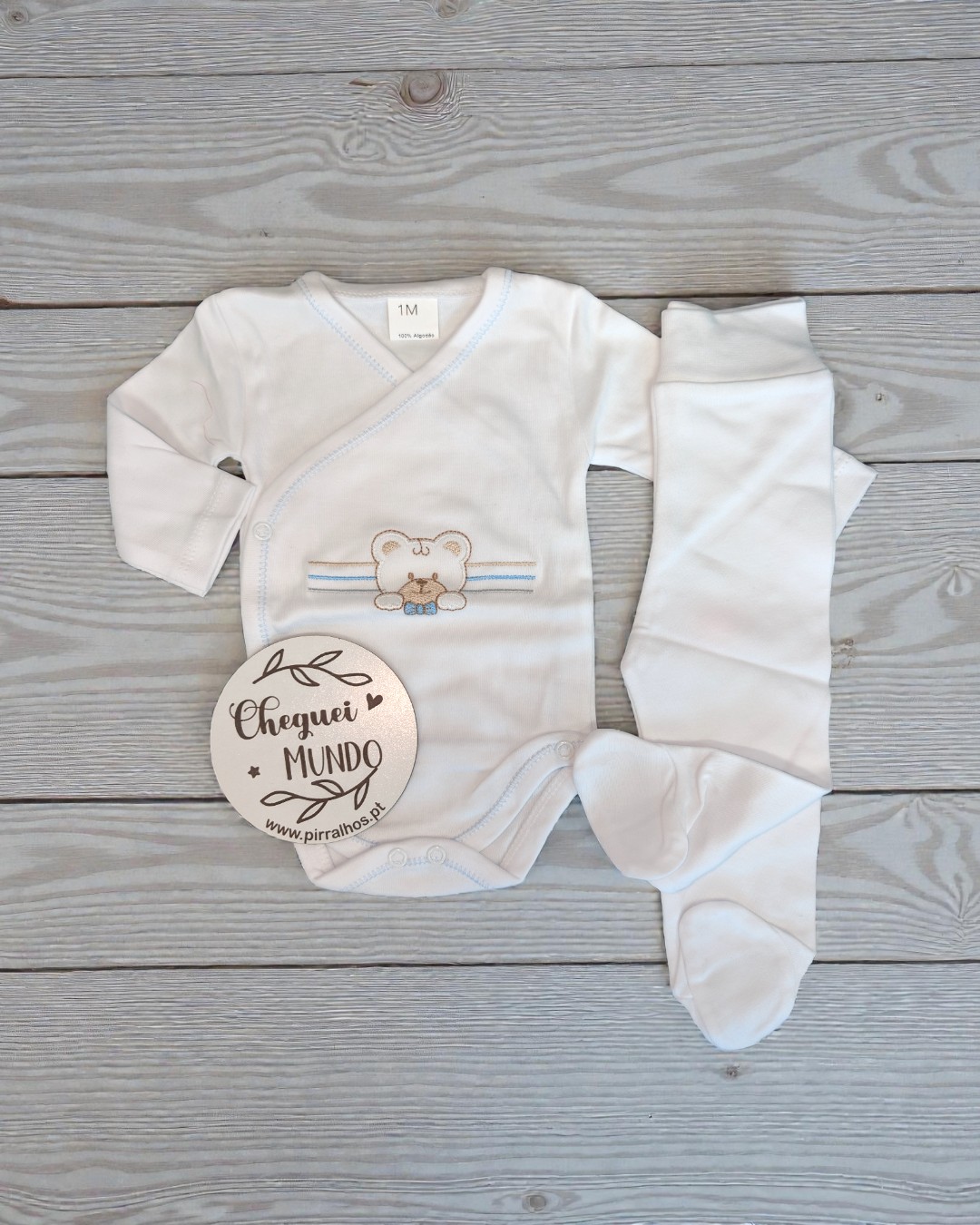 Conjunto de roupa de bebé branco com bordado e etiqueta em madeira clara