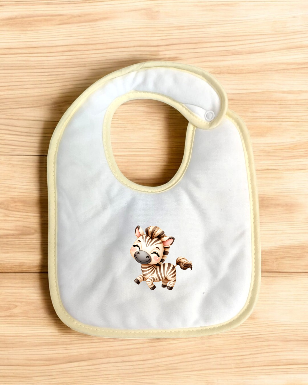 Babete branco com borda amarela e desenho de zebra sobre madeira clara