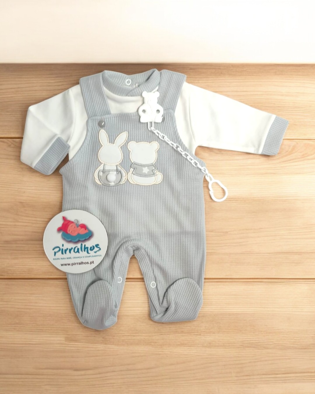 Conjunto de bebé cinza com macacão e body branco sobre fundo de madeira