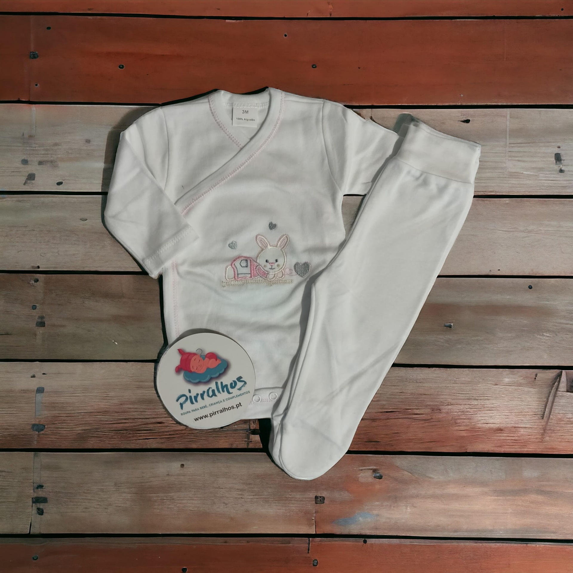 Conjunto de roupa branca para bebé com bordado de coelho sobre fundo de tábuas de madeira