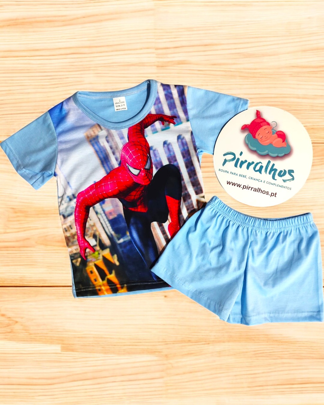 Conjunto infantil azul com estampa Spider-Man em fundo de madeira clara e etiqueta Pirralhos