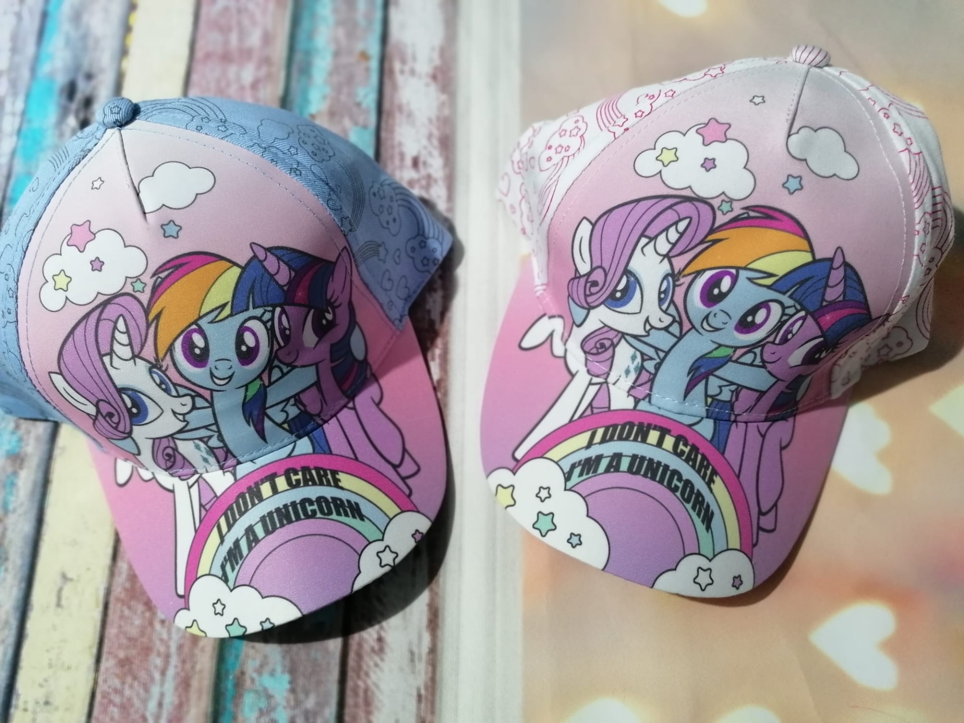 Dois bonés infantis coloridos com desenhos de personagens de desenho animado e arco-íris