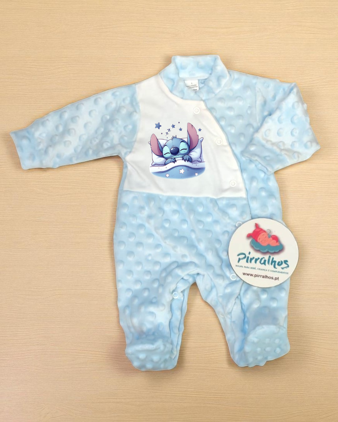 Macacão azul claro com estampa de personagem e etiqueta redonda em superfície de madeira clara