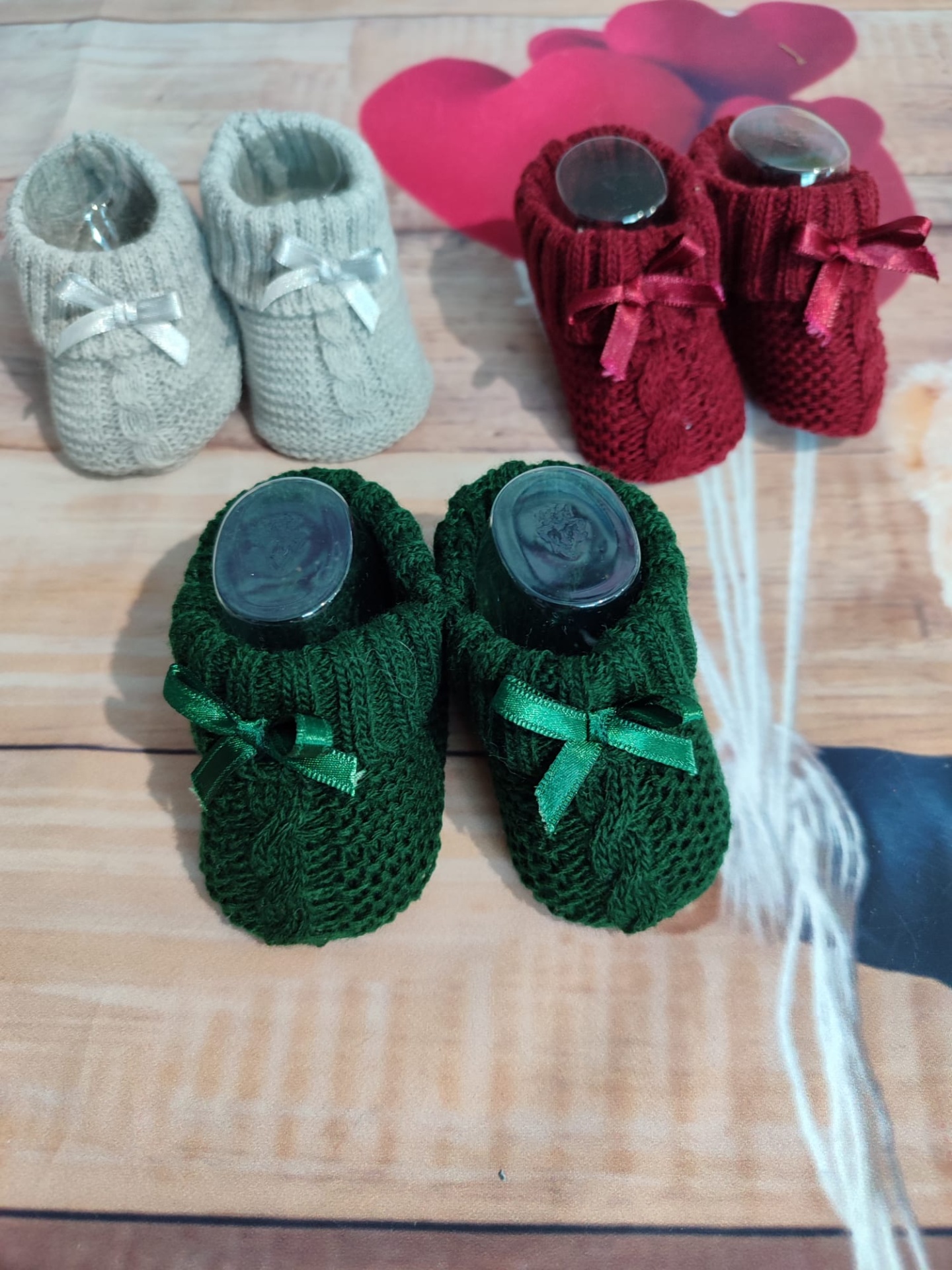 Três pares de sapatinhos de bebé de malha em diferentes cores sobre madeira clara com decoração de balões