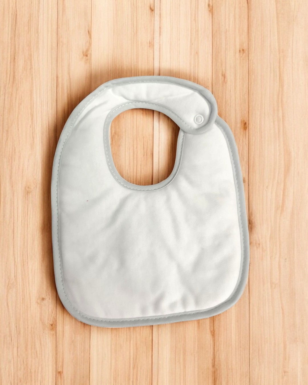 Babete de bebé branco com borda cinzenta sobre fundo de madeira