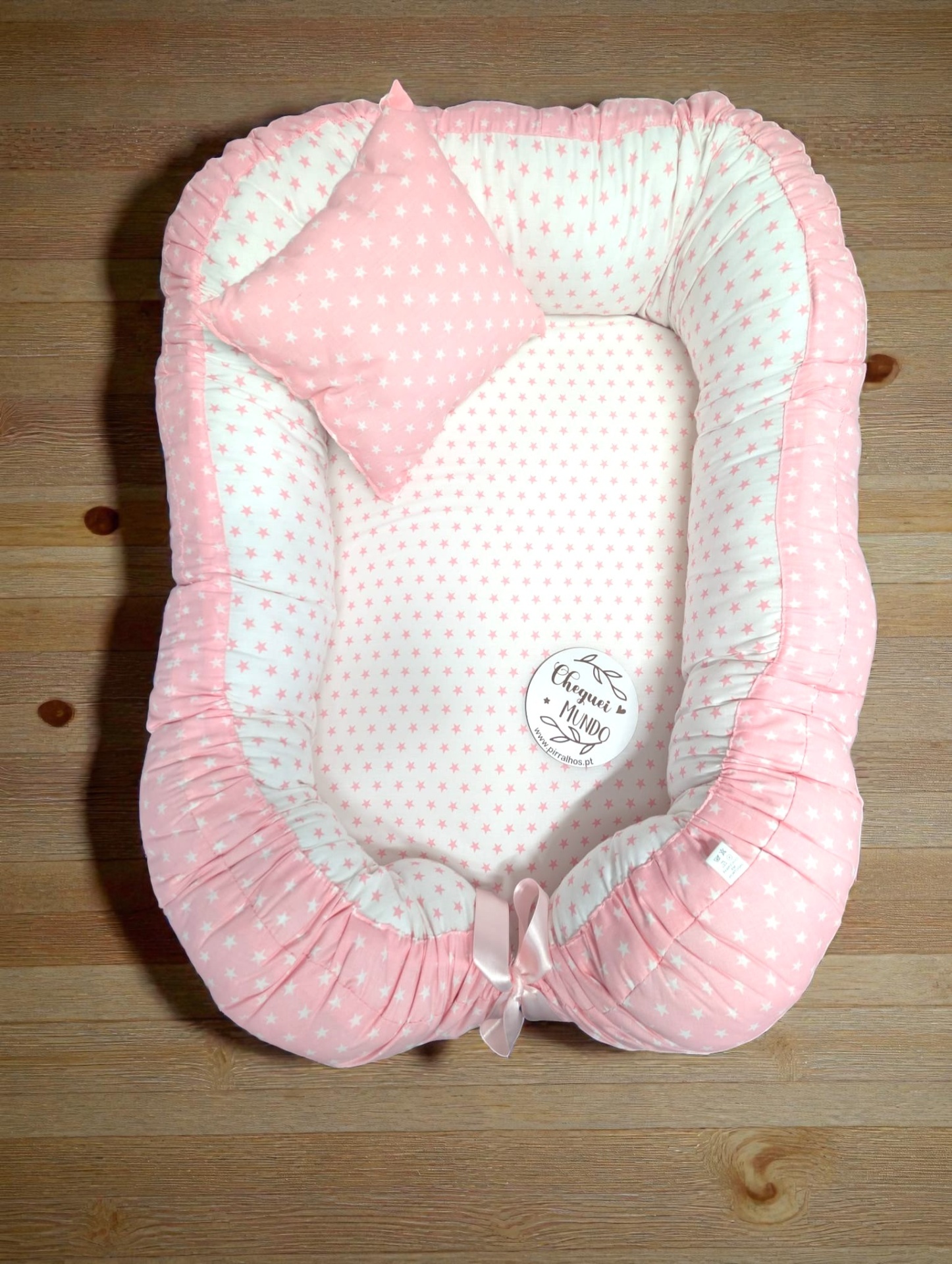 Ninho para bebé rosa e branco com estrelas e almofada em chão de madeira