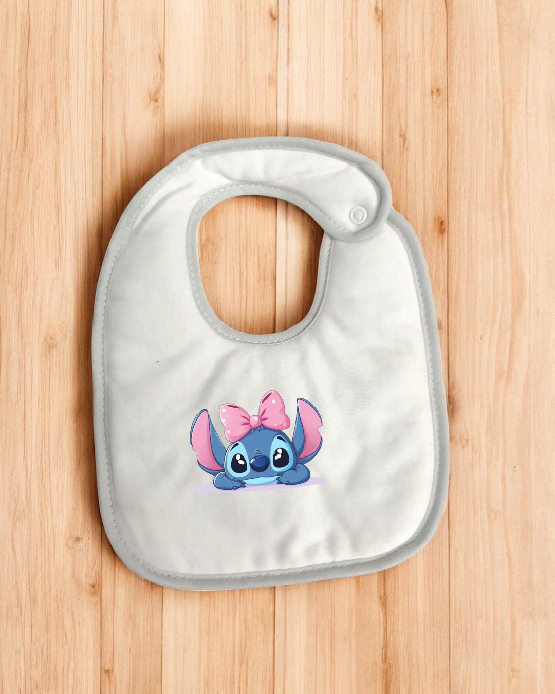 Babete branco com personagem azul e laço cor-de-rosa, colocado sobre madeira clara