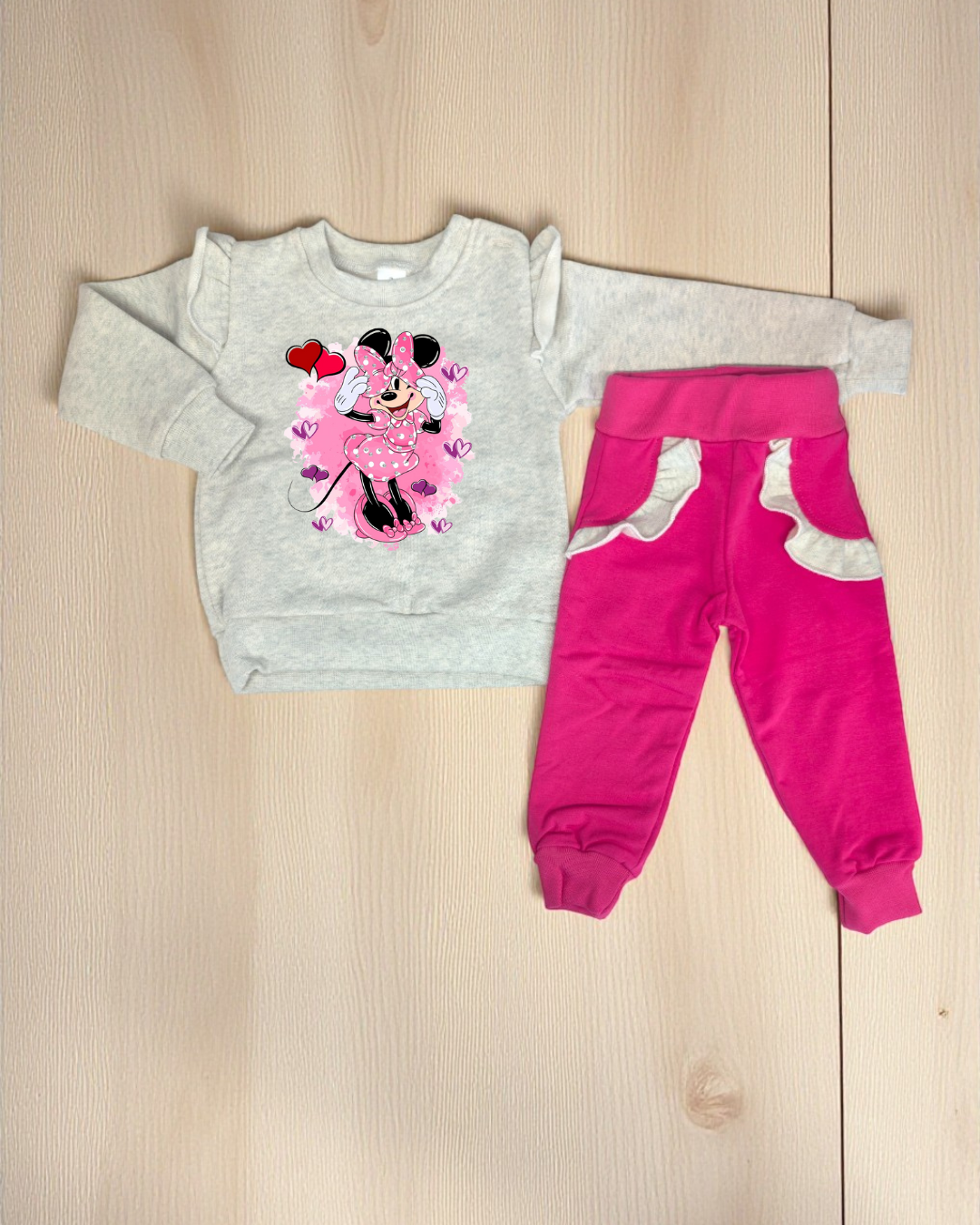 Conjunto de roupa infantil com camisola cinzenta e calças cor de rosa com detalhes em branco no chão de madeira clara
