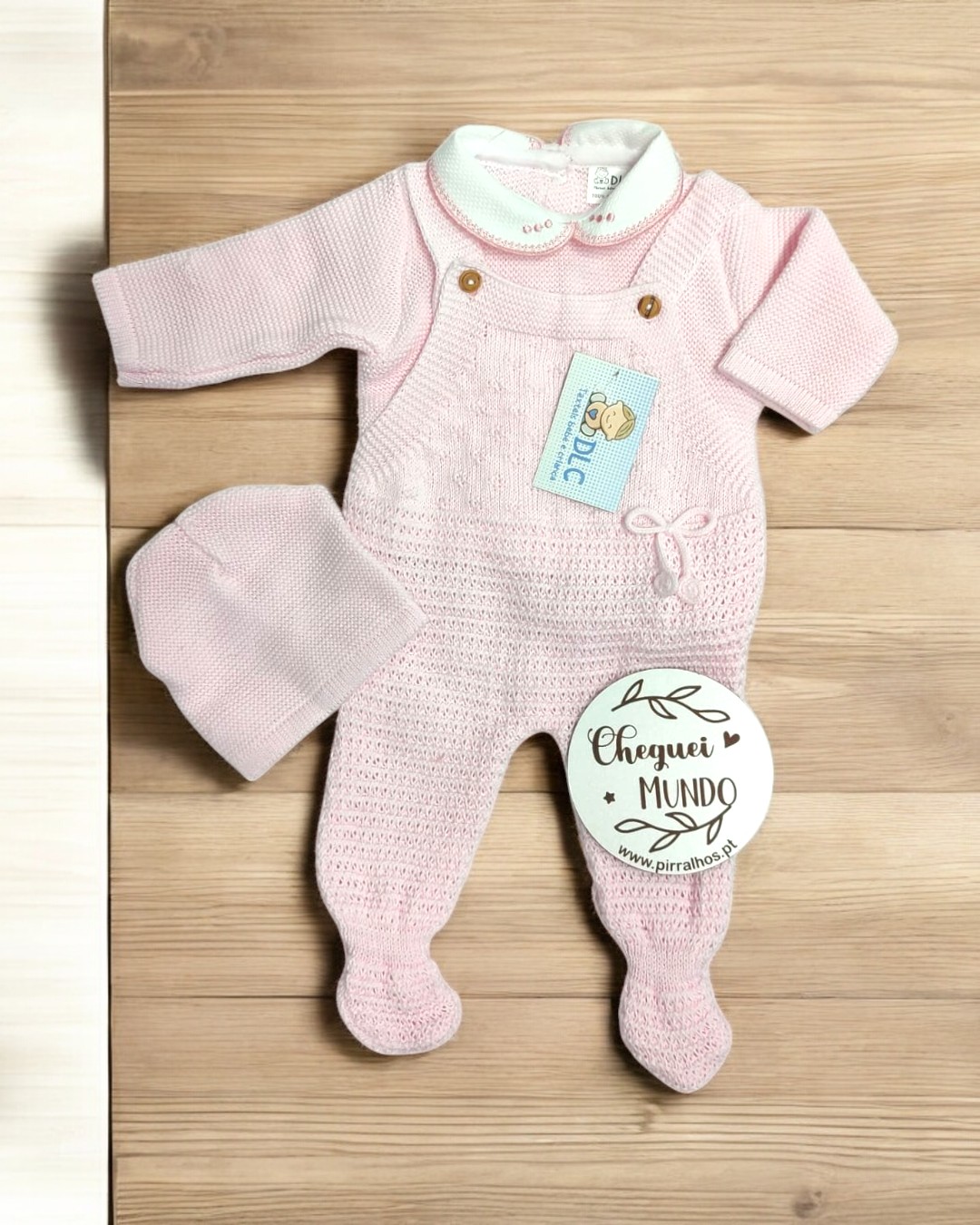 Conjunto de roupa de bebé rosa clara com macacão e gorro em malha, sobre fundo de madeira clara