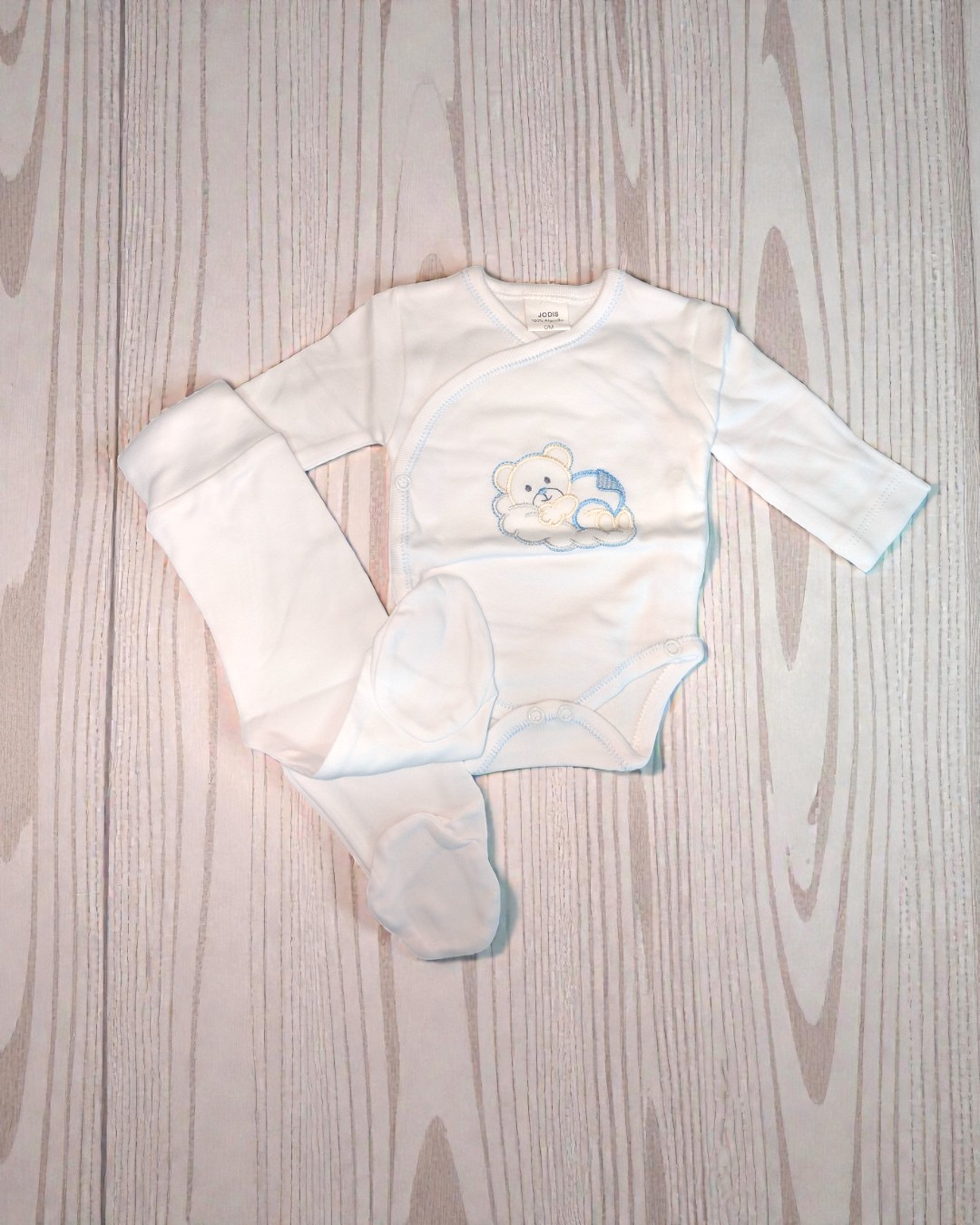 Conjunto de roupa de bebé branca com body e calças com pés sobre fundo de madeira clara