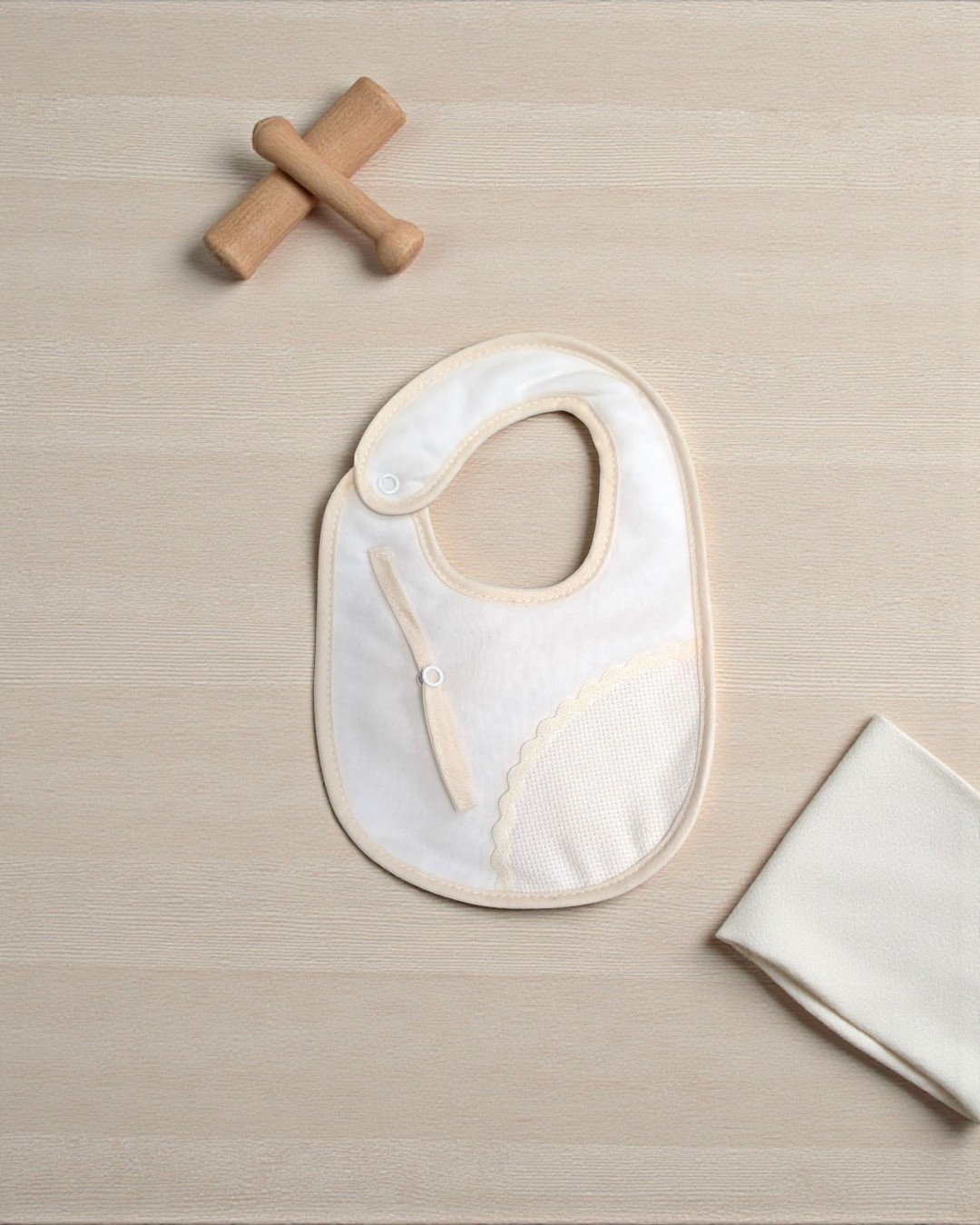 Babete branco com bordas bege e um brinquedo de madeira