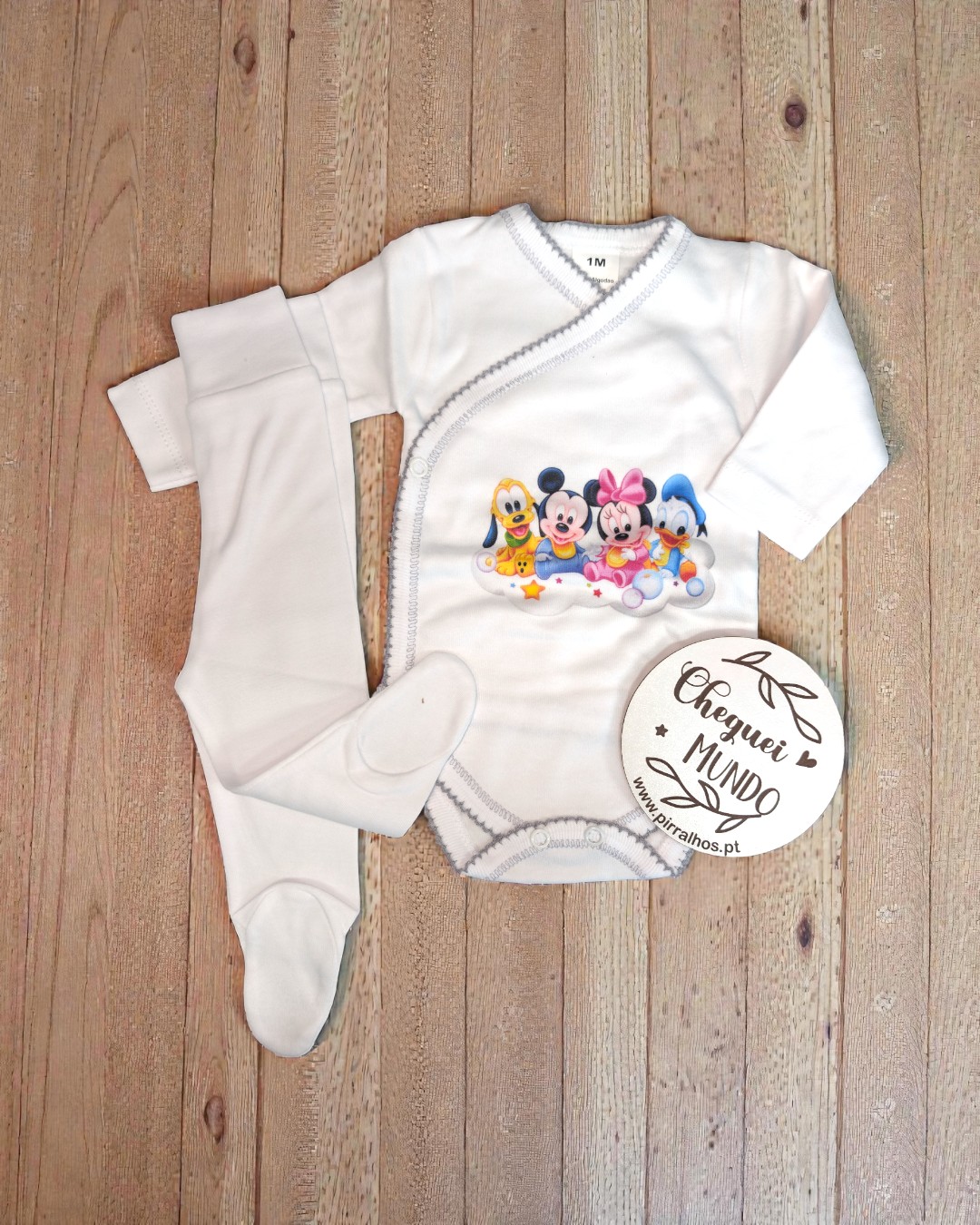 Conjunto de roupa de bebé branca com personagens Disney, mostrado sobre madeira.