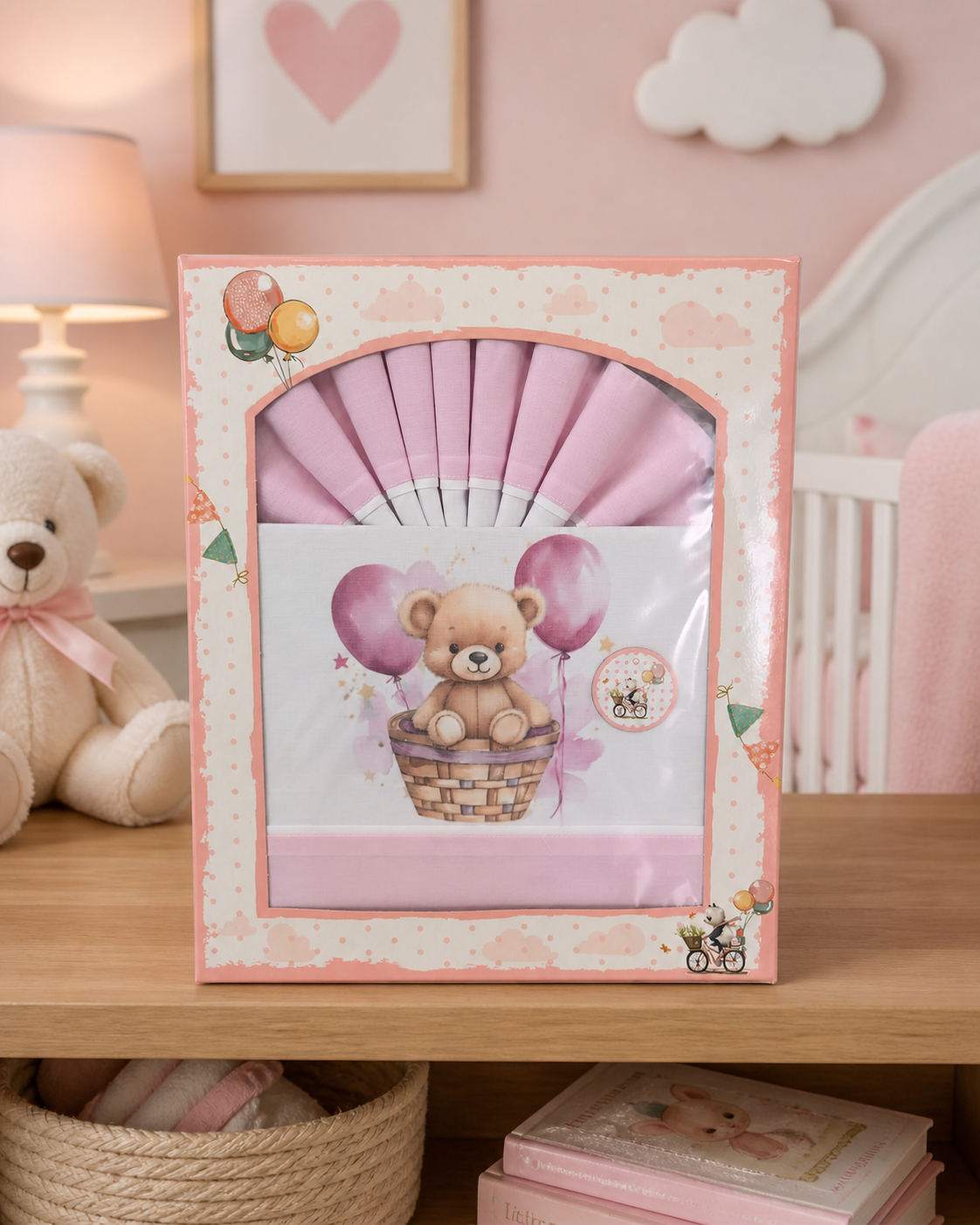Jogo de cama infantil rosa com ursinho e balões na embalagem colocada numa mesa de madeira num quarto cor-de-rosa