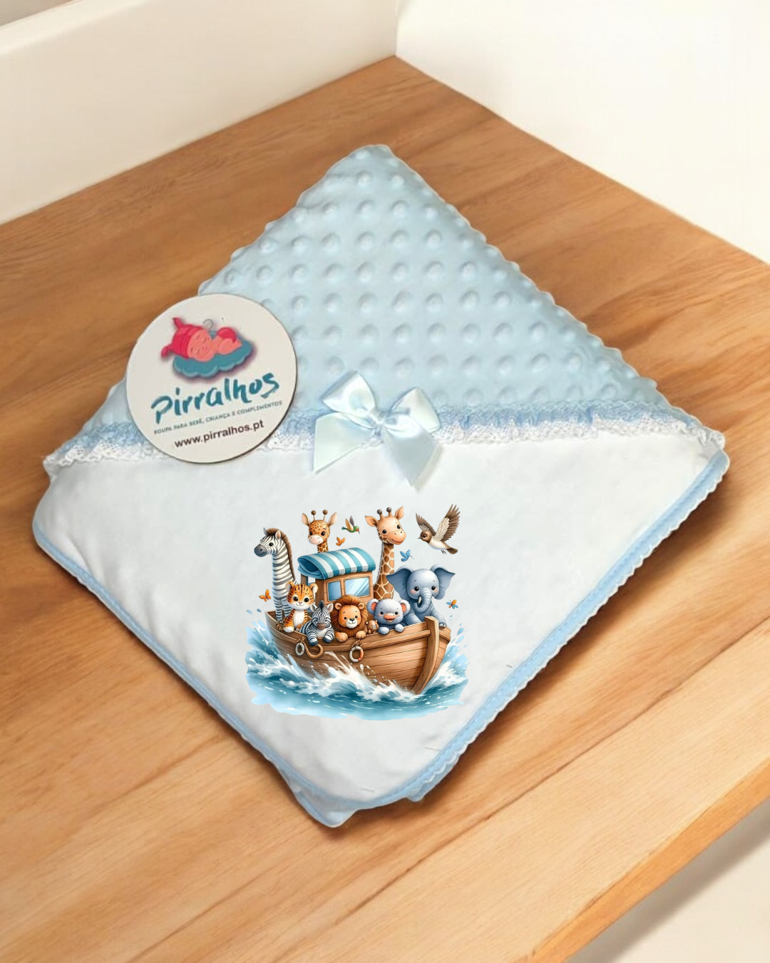 Manta azul para bebé com estampa de animais e etiqueta Pirralhos sobre mesa de madeira