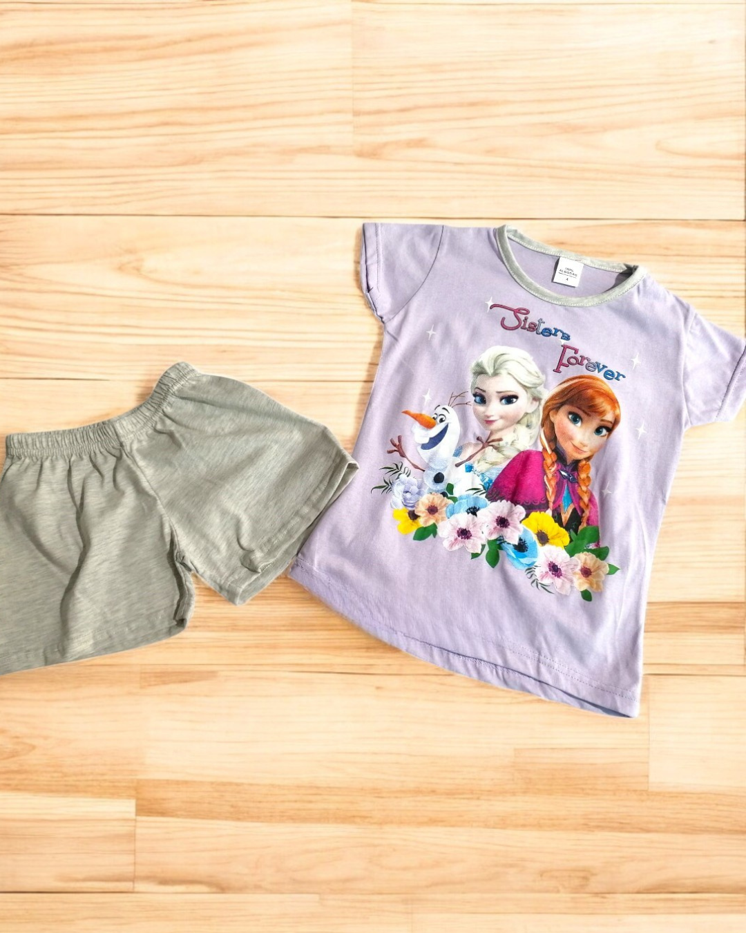 Conjunto infantil t-shirt lilás Frozen e calções cinza claro sobre chão de madeira
