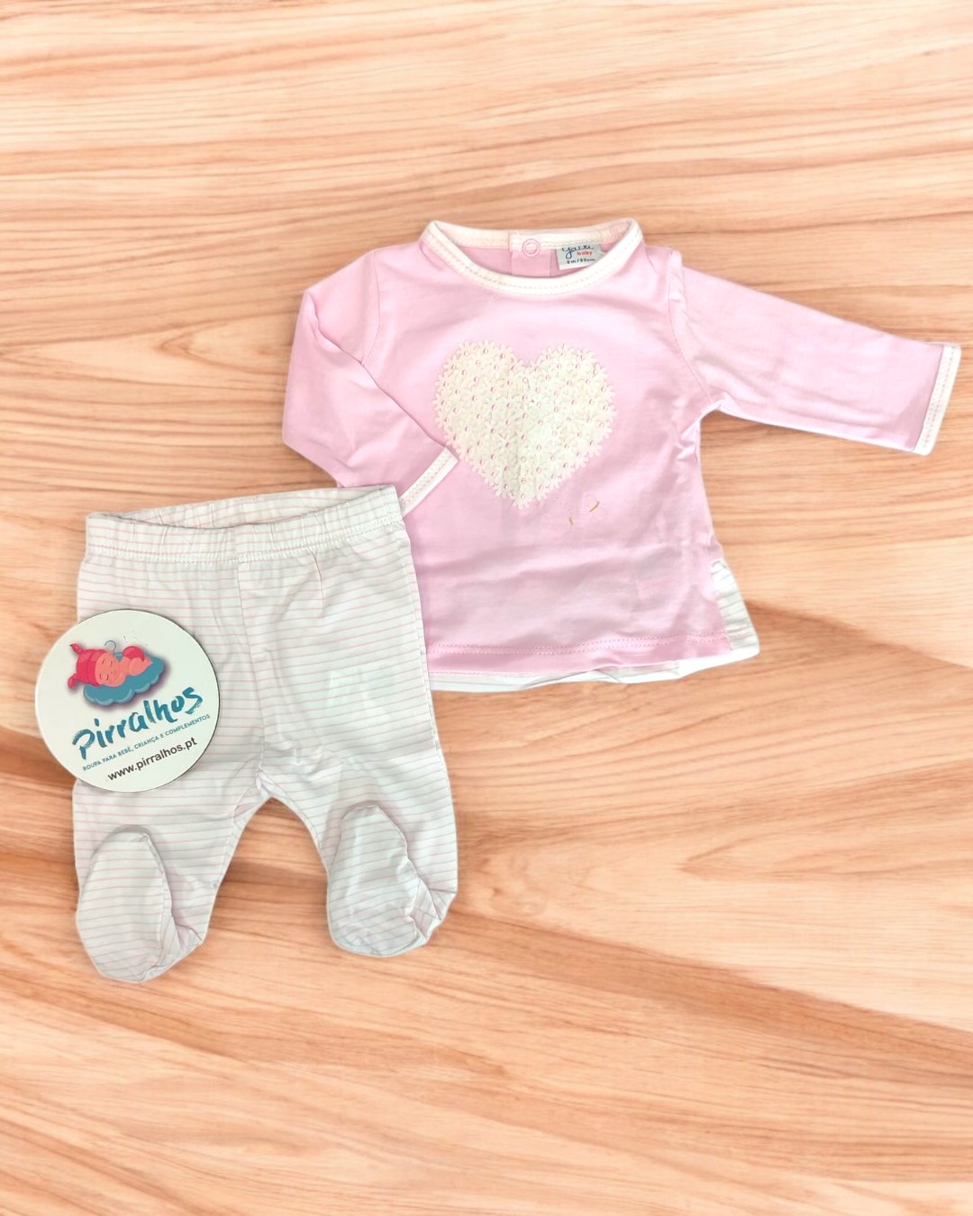 Conjunto de roupa de bebé rosa e branca com coração e riscas sobre madeira