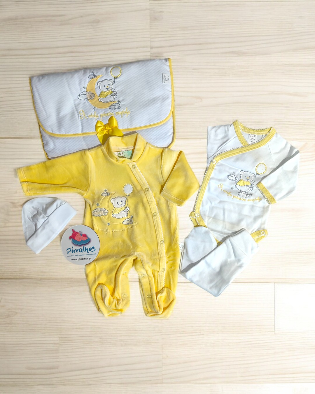 Conjunto de roupas para bebé amarelas e brancas com ursinho bordado e saco de transporte.