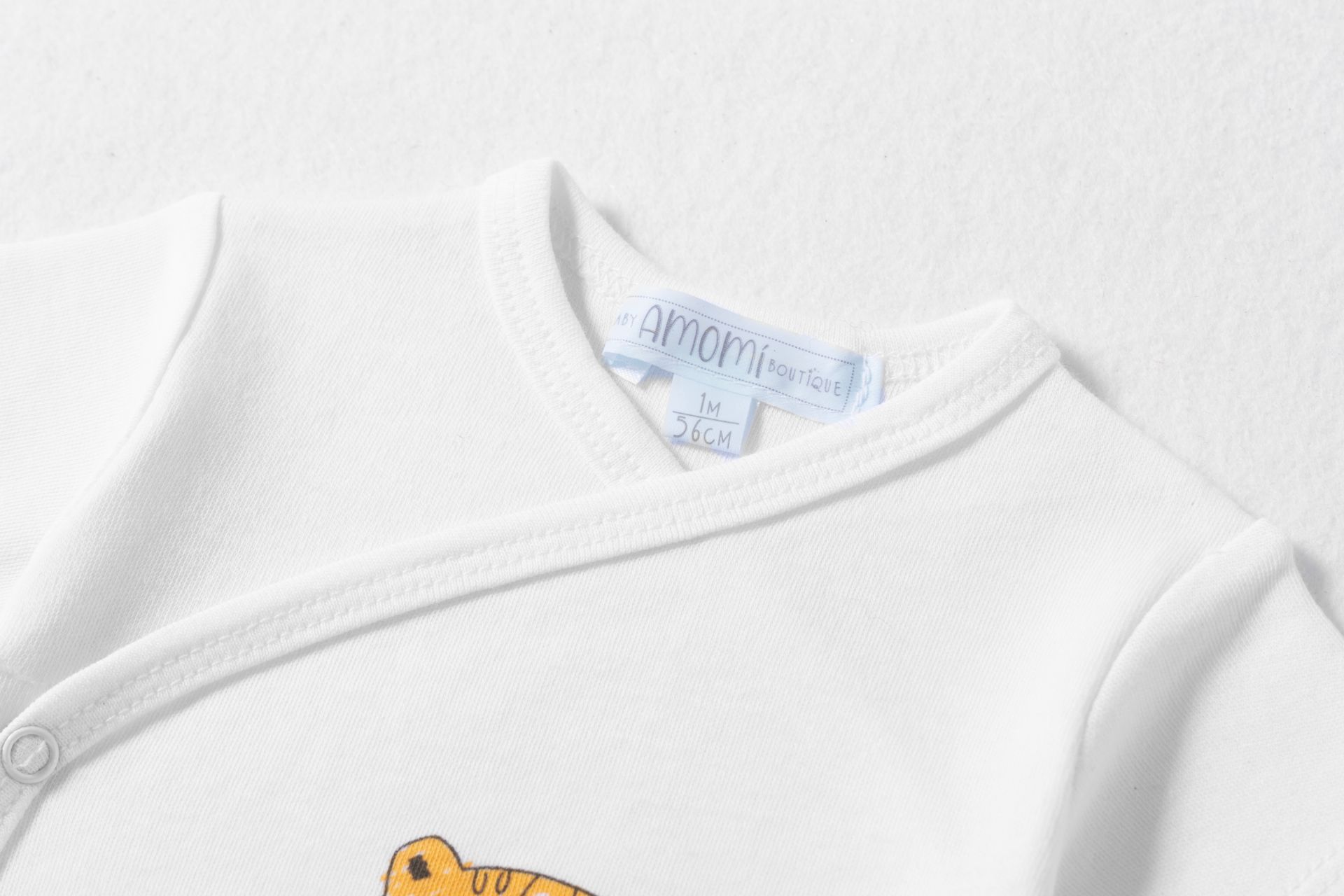 Roupas de bebé brancas com bordado de tigre e etiquetas visíveis.