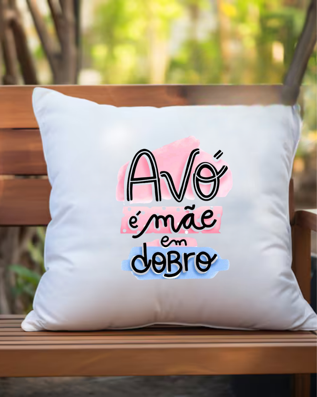 Almofada branca com texto colorido 'Avó é mãe em dobro' num banco de madeira ao ar livre