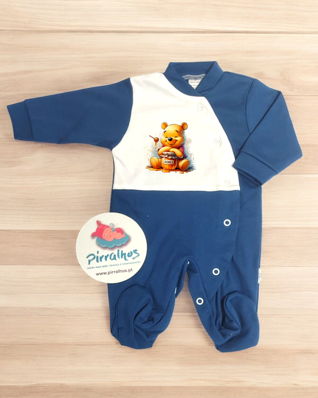 Macacão de bebé azul e branco com estampa do Ursinho Pooh, botões de pressão e fundo de madeira clara