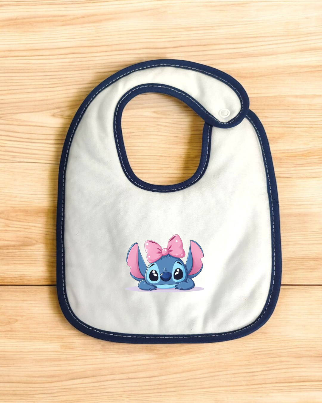 Babete branco com borda azul escura e personagem azul com laço cor-de-rosa