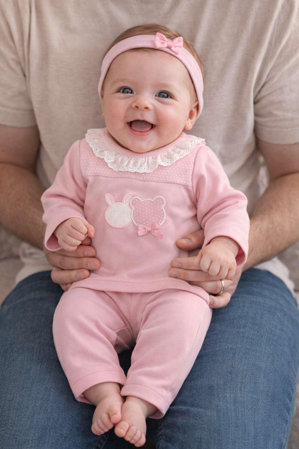 Bebé sorridente com roupa rosa sentada no colo de um adulto.
