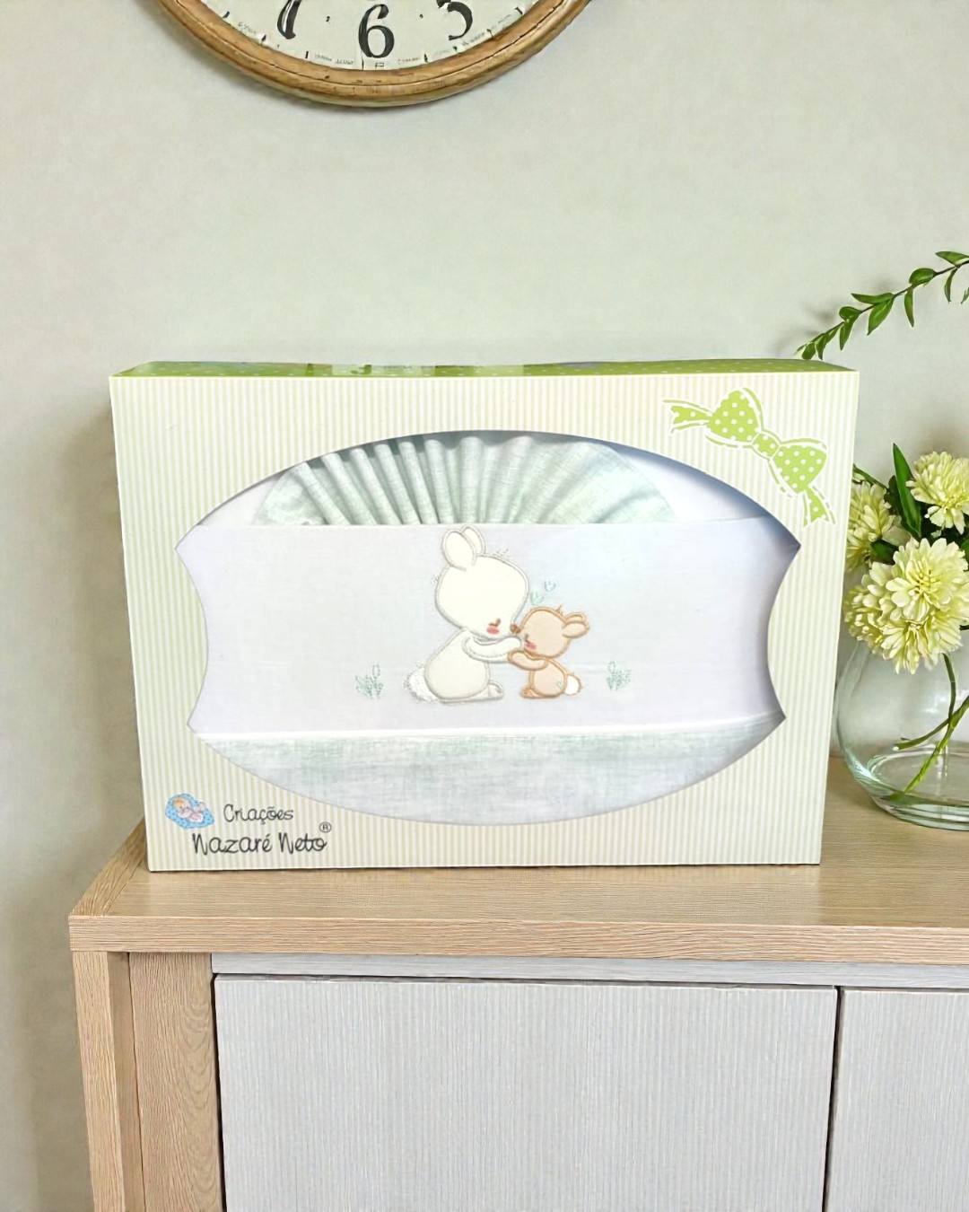 Conjunto para bebé branco e cinza claro com bordado de coelhinhos em caixa decorada verde sobre móvel de madeira
