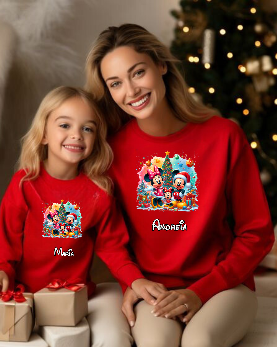Duas pessoas com sweats vermelhas da Disney com nomes personalizados, ao lado de presentes e árvore de Natal.