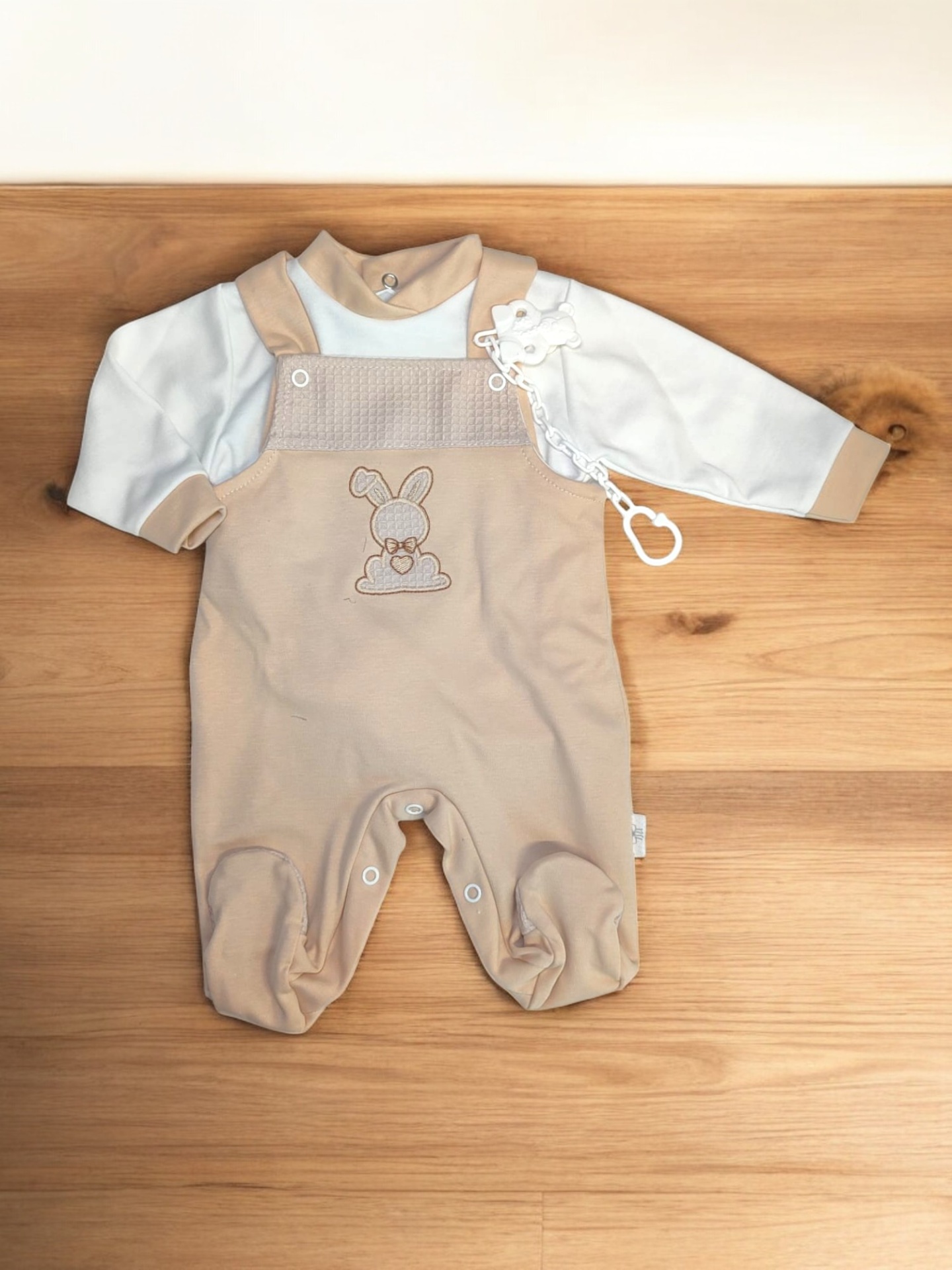 Fato de bebé creme e bege com bordado de coelho colocado sobre madeira