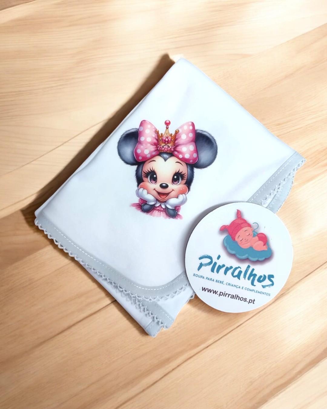 Lenço branco com estampa Minnie Mouse e cartão Pirralhos sobre mesa de madeira clara