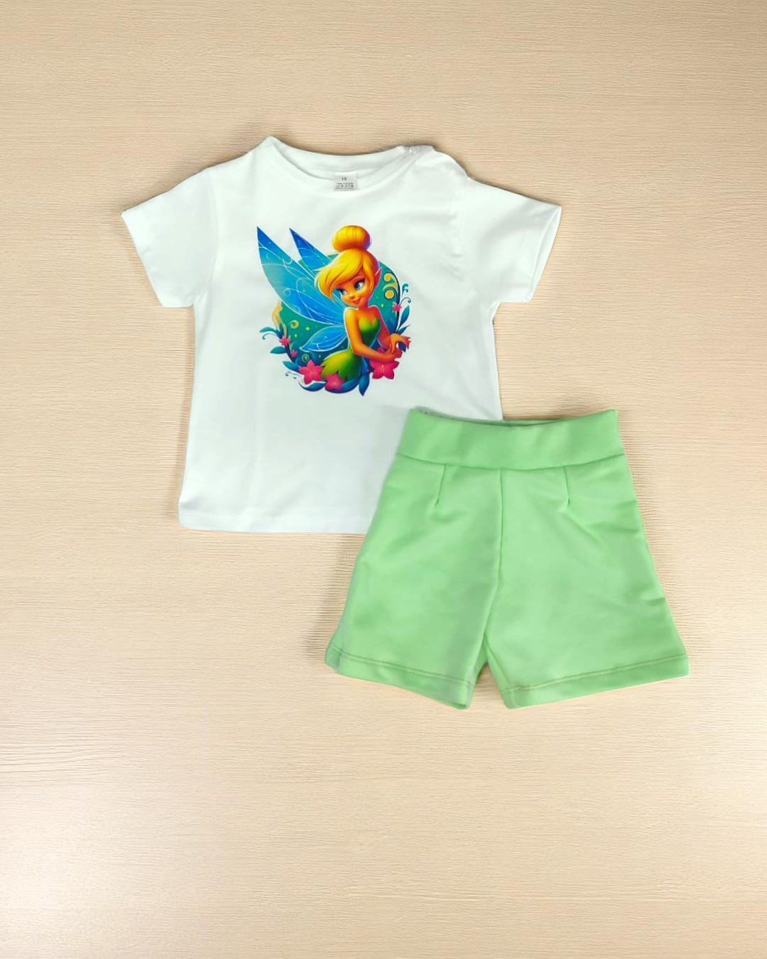 Conjunto infantil com t-shirt branca com estampa de fada colorida e shorts verdes claros.