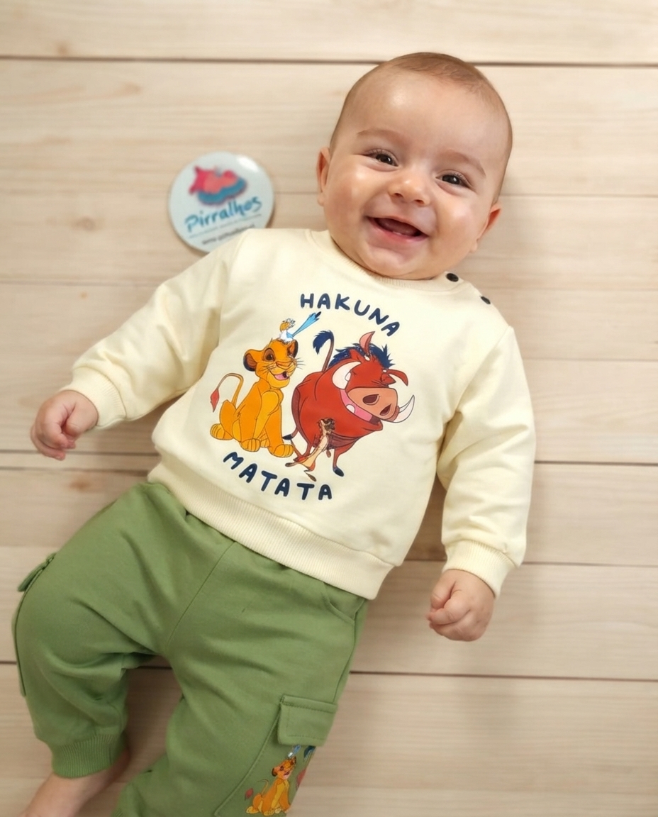Bebé a sorrir com camisola creme com personagens e calças castanhas com bolsos