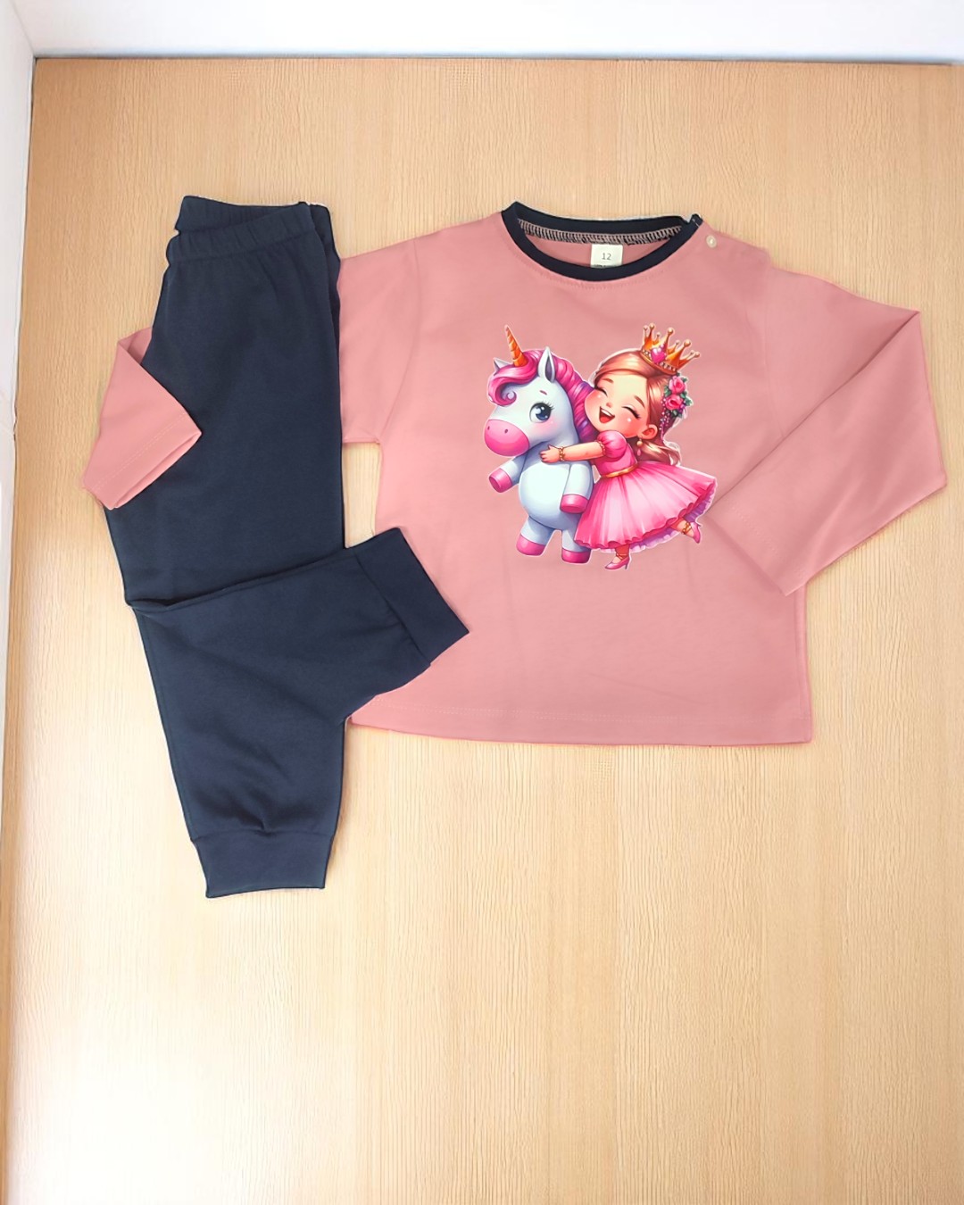 Conjunto de roupa infantil com camisola rosa estampada e calças pretas.