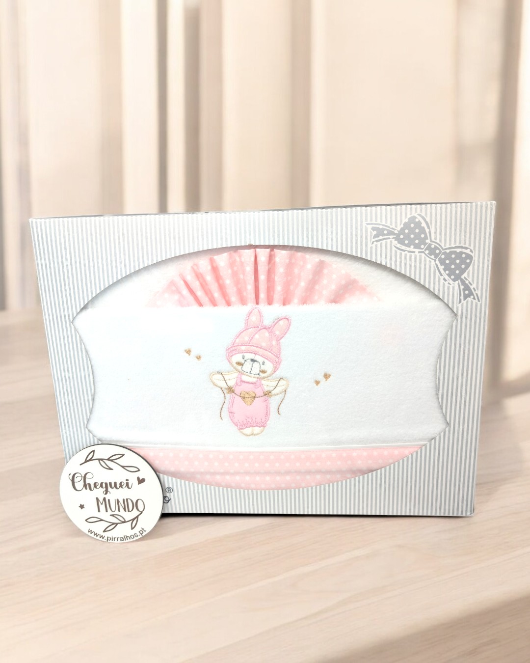 Manta branca e rosa com ilustração de coelho em embalagem cinza com riscas