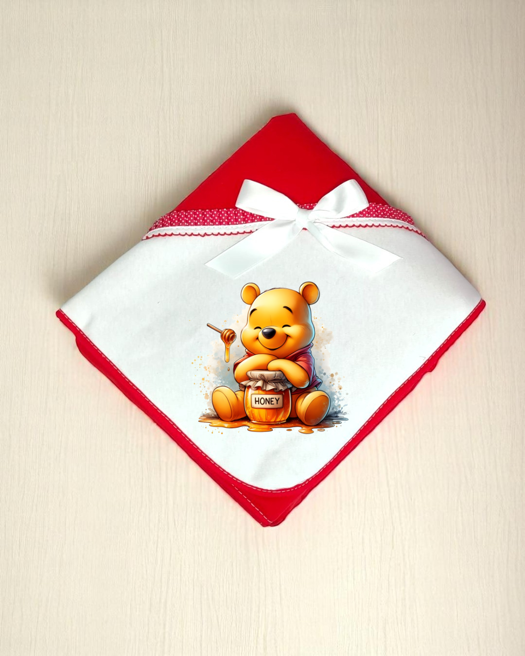 Manta branca e vermelha com imagem do urso Winnie the Pooh e pote de mel.