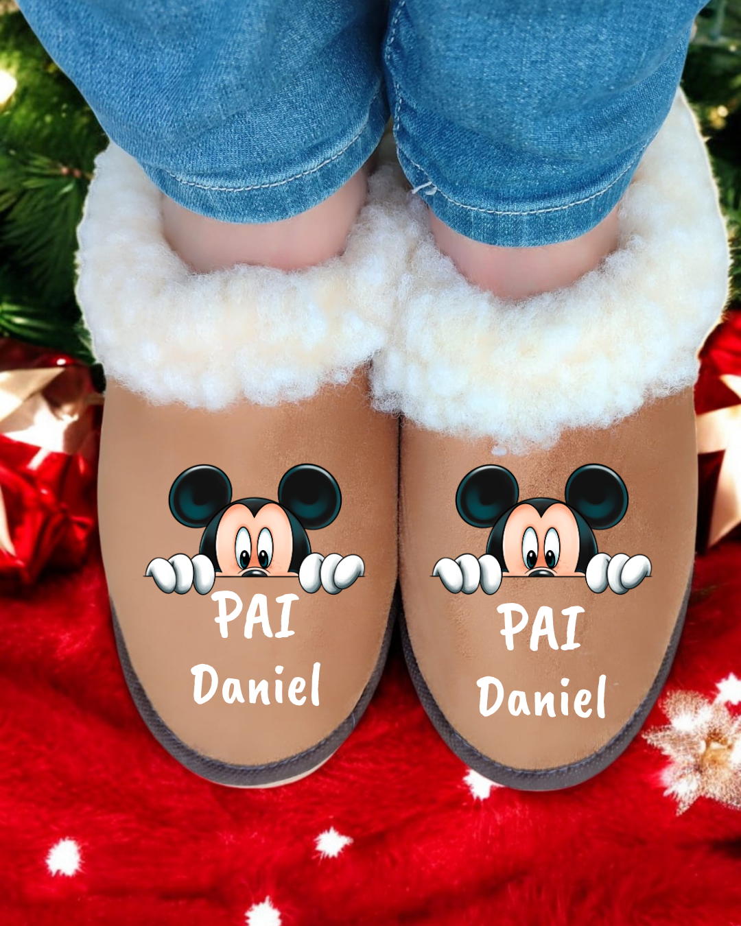 Chinelos marrons com pelo branco e desenho do Mickey Mouse, texto 'PAI Daniel', usados por pessoa com calças de ganga, fundo vermelho de Natal